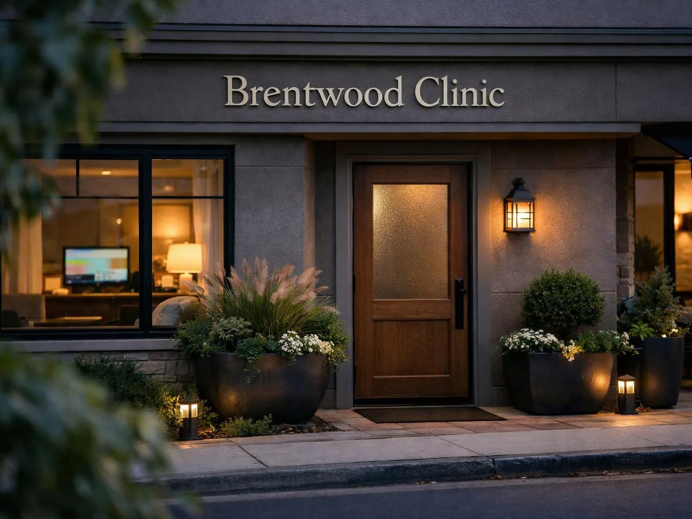 A clinic entrance at dusk shows a wooden door, lit windows, potted plants, and a glowing wall lantern