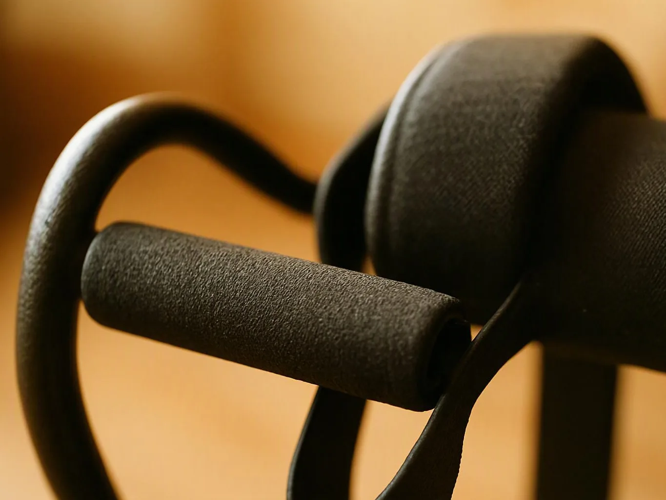 Close-up of a black padded handle and curved metal frame against a warm blurred background