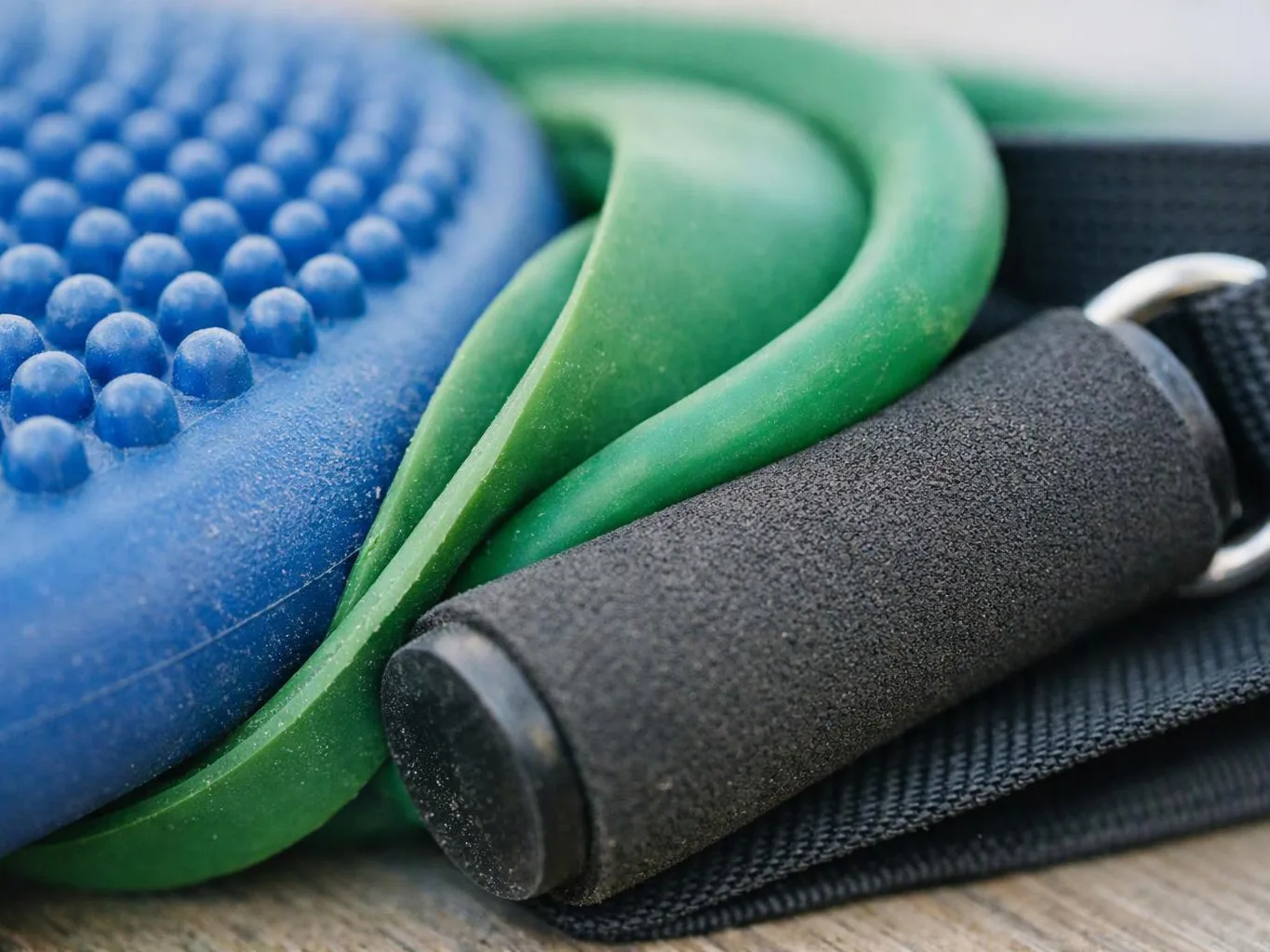 Close-up of blue, green, and black exercise grips and bands on a wooden surface