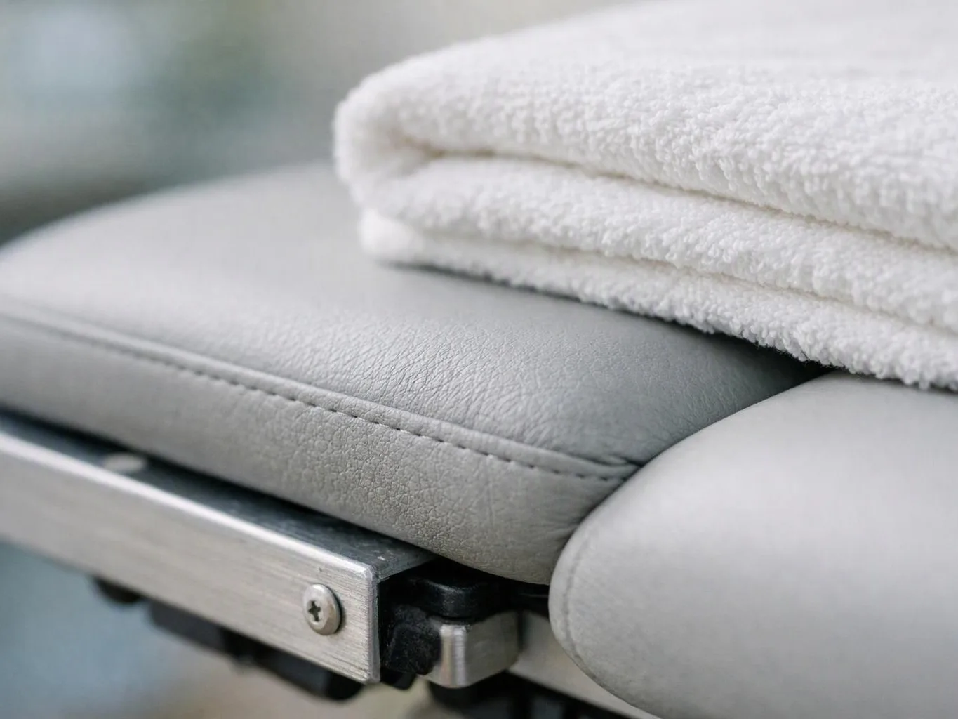 A folded white towel rests on a gray leather cushion with a metal frame below