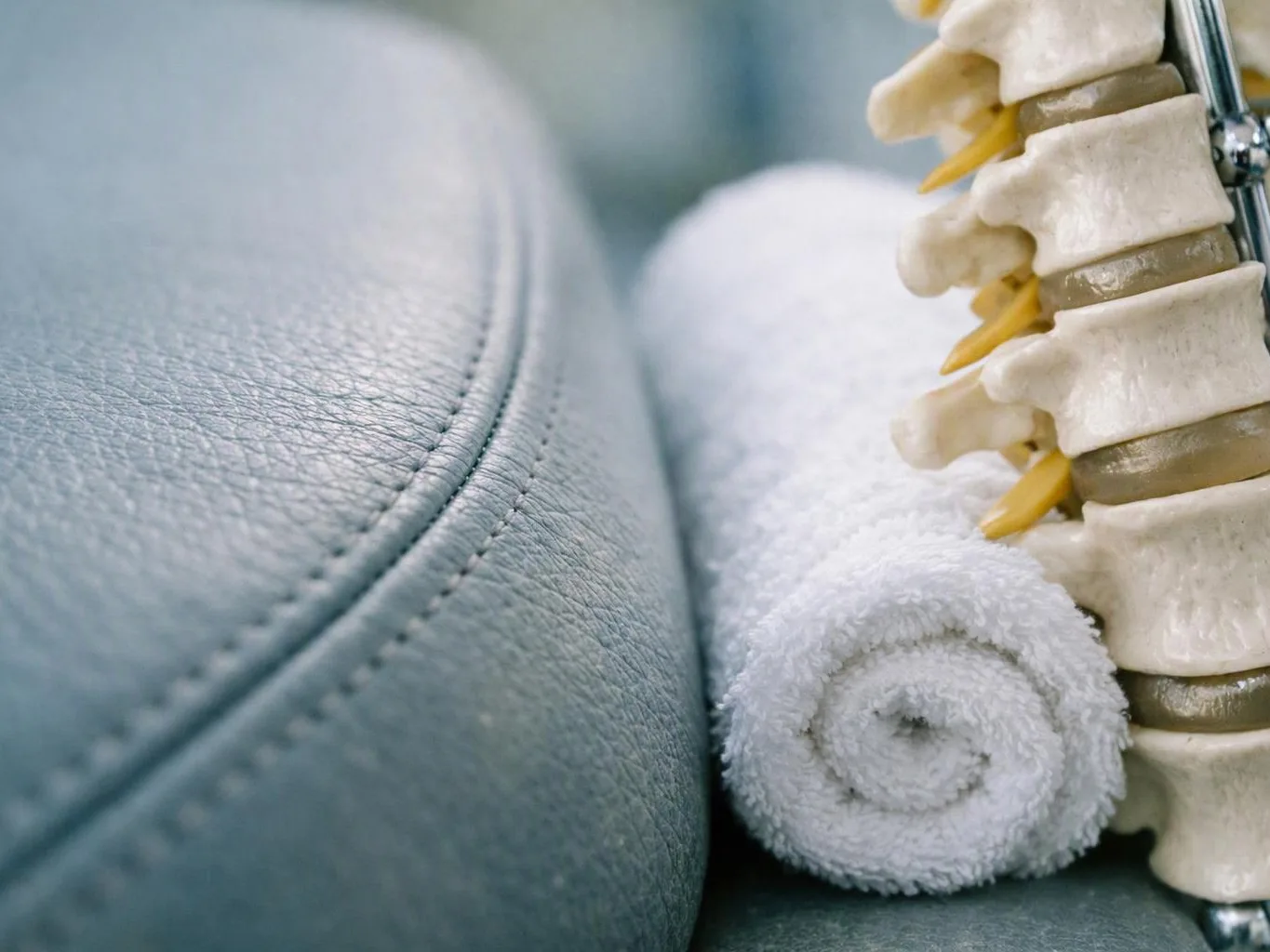 A rolled white towel rests beside a spine model on a blue padded table